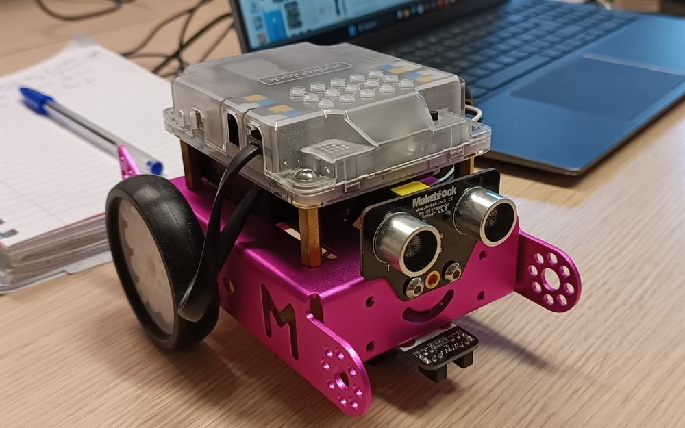 Un petit robot programmable à roues, ses capteurs à l'avant, posé devant l'ordinateur qui le pilote.
